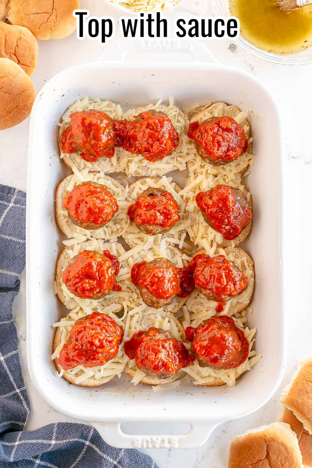 a white baking dish with slider bun bottoms, cheese meatballs and sauce.