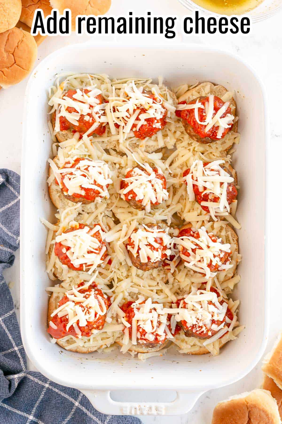 a white baking dish with slider bun bottoms, cheese meatballs and sauce, topped with more cheese.