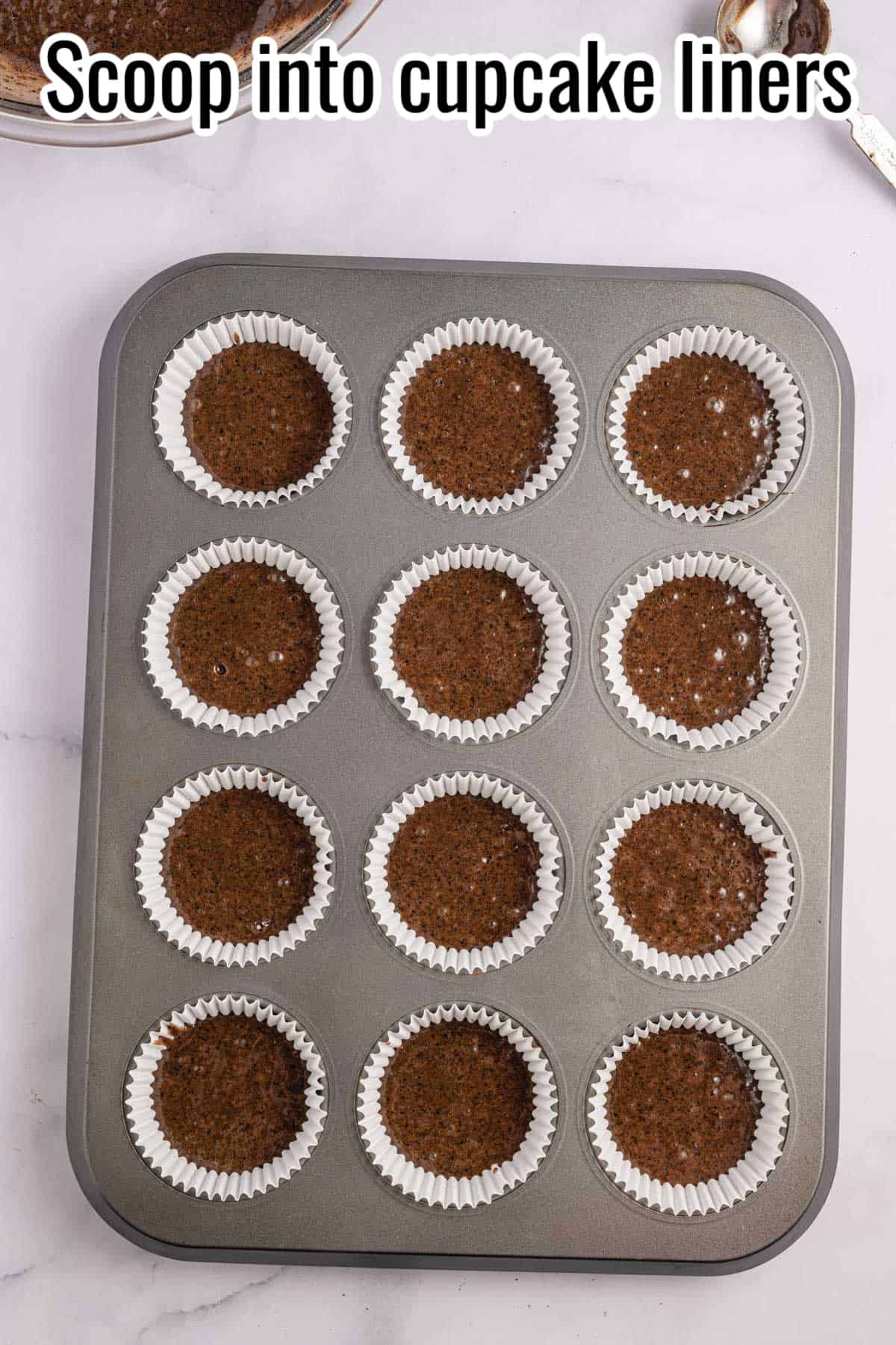 Chocolate cupcakes in a muffin tin with the word "Scoop into cupcake liners".