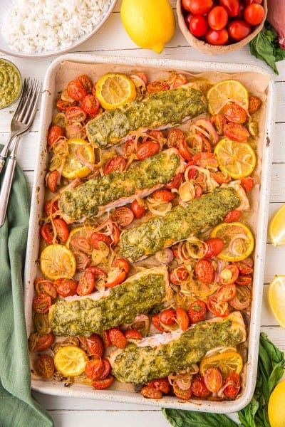 pesto salmon on a sheet pan with lemons and tomatoes.