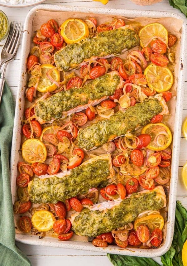 pesto salmon on a sheet pan with lemons and tomatoes.