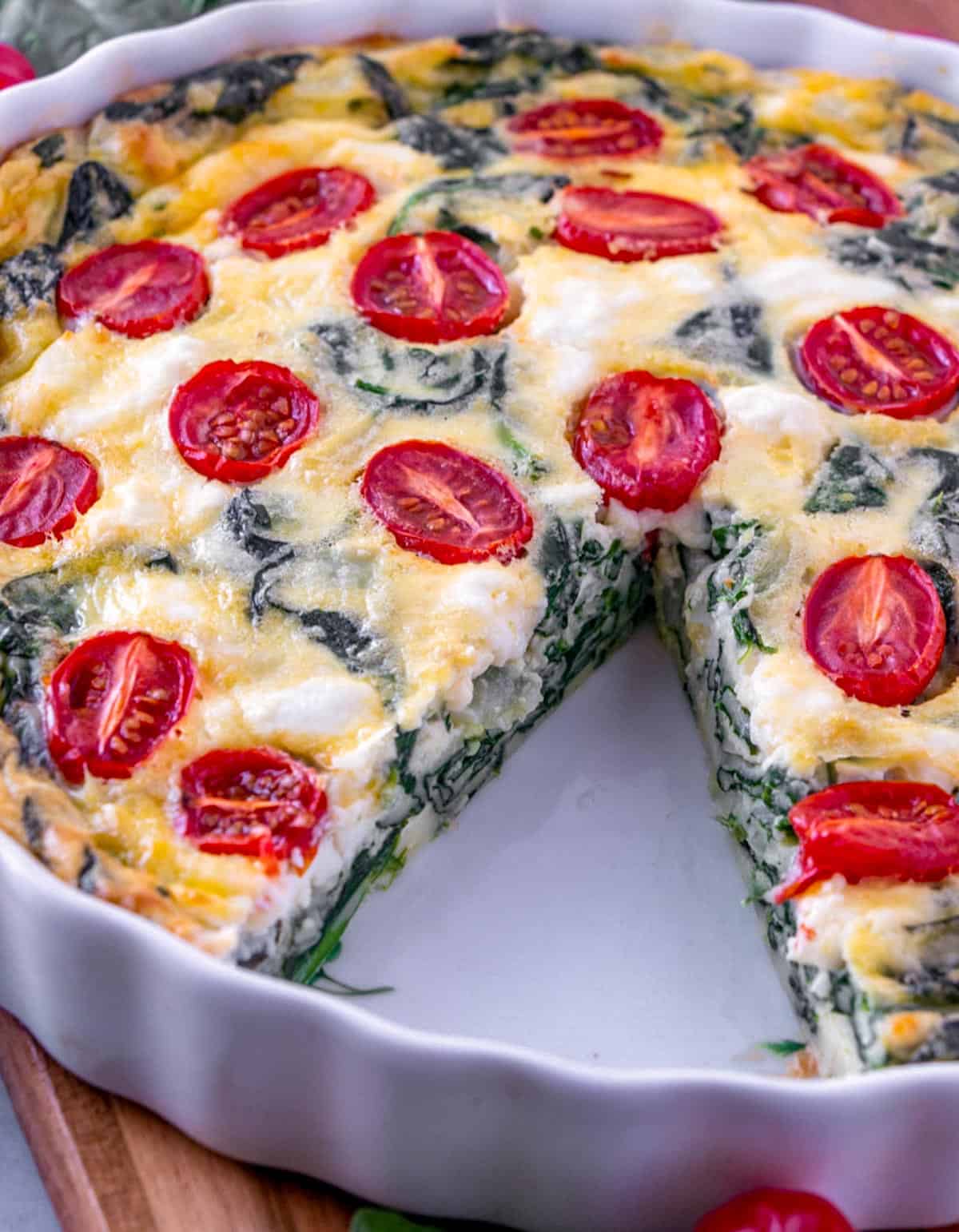 spinach quiche in a white tart pan, with a slice taken out.