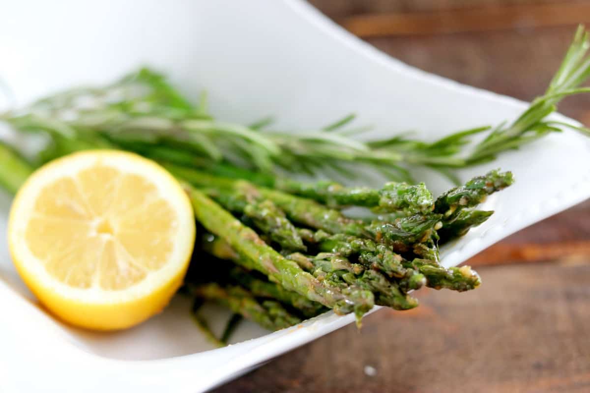 asparagus with lemon and rosemary in a white dish.