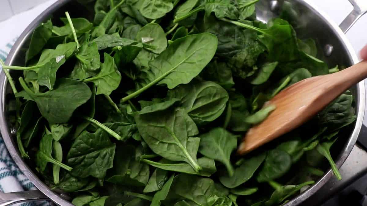 fresh spinach in a skillet with a wooden spoon.