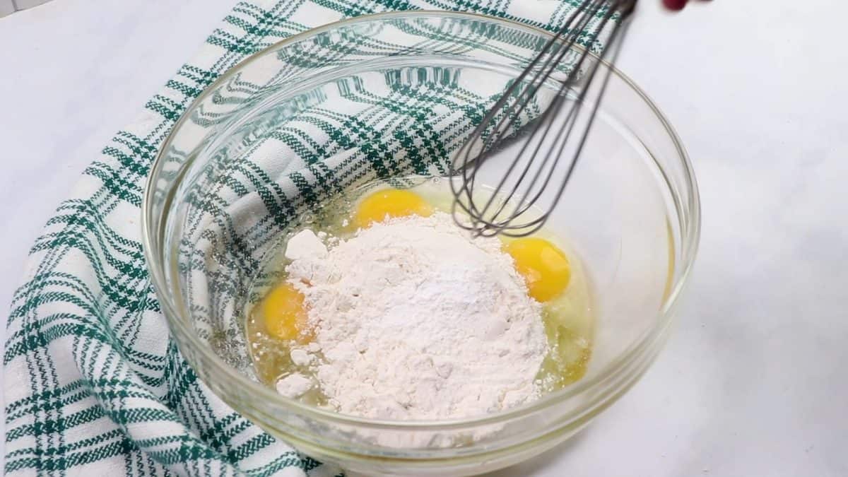 eggs and flour in a glass bowl with a whisk.