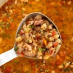 A ladle of bean and vegetable soup with herbs and chunks of meat.