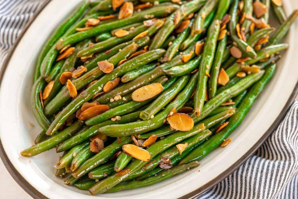 Green beans garnished with toasted almond slices on a white oval plate.