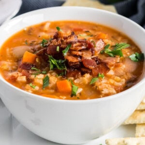 A bowl of lentil soup topped with crispy bacon and fresh parsley.