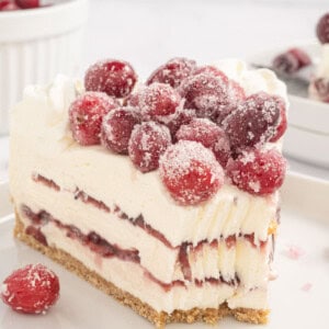 A slice of Christmas cheesecake with a graham cracker crust, creamy filling, cranberry sauce, and sugared cranberries on top.