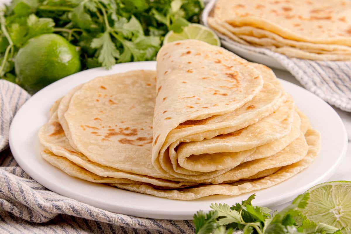 Soft homemade flour tortillas stacked on a plate