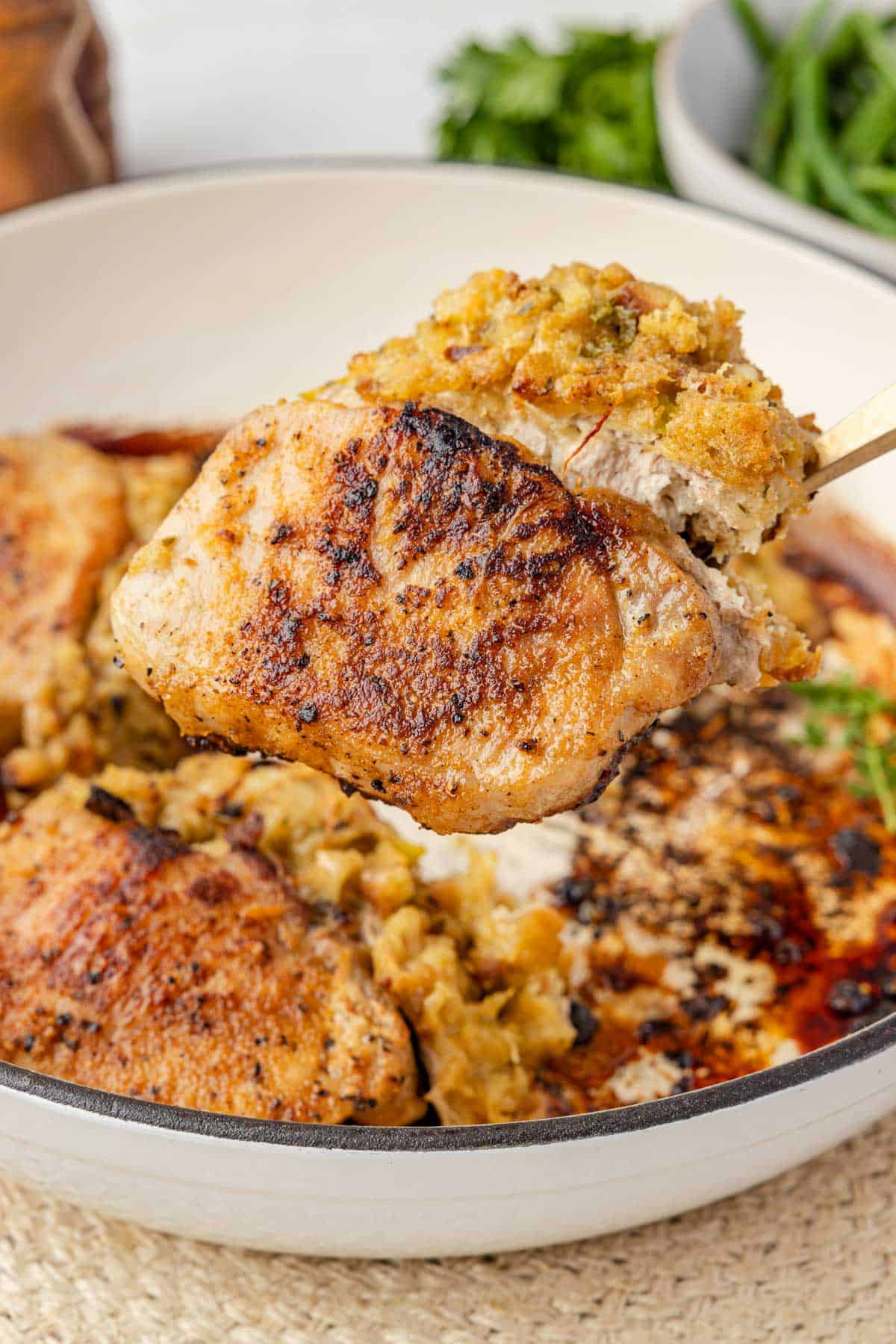 A pork chop stuffed with seasoned bread mixture being lifted from the skillet.