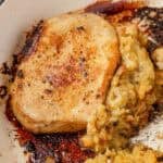 A golden brown pork chop in a skillet beside fluffy bread stuffing.