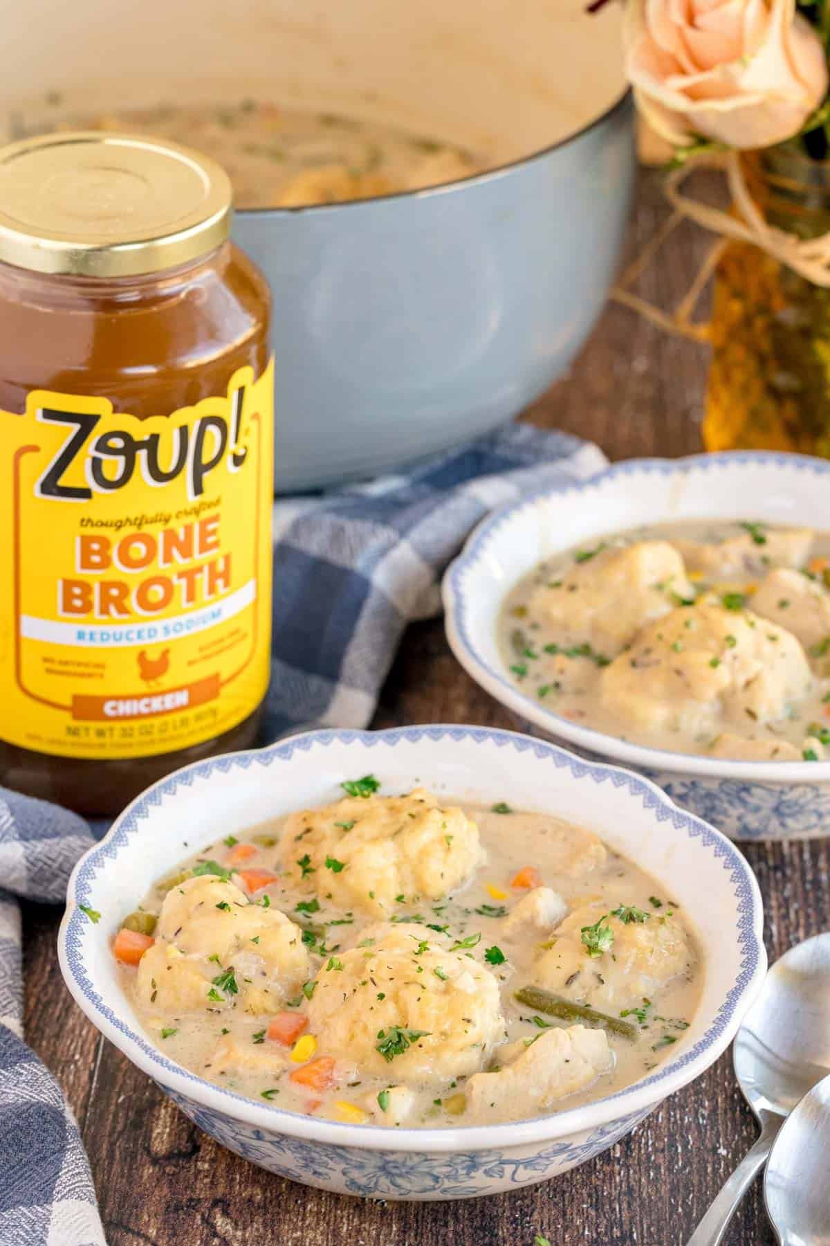 A jar of Zoup! chicken bone broth next to two bowls of chicken and dumplings.