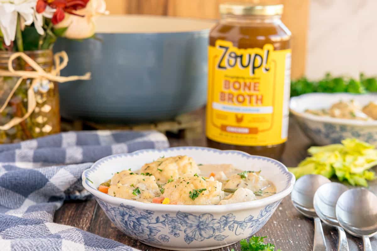 A bowl of chicken and dumplings in front of a jar of Zoup! bone broth and a Dutch oven.