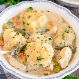 A bowl of chicken and dumplings with mixed vegetables in creamy broth.