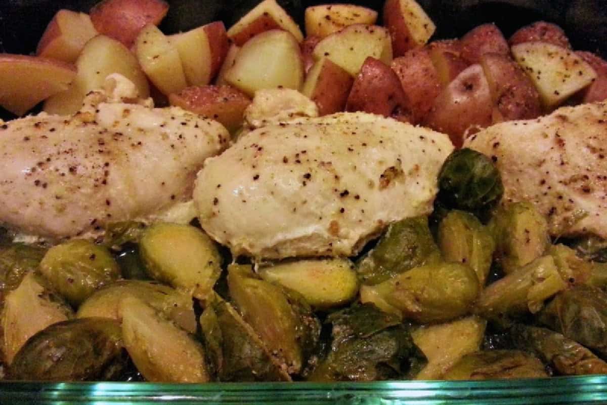 Italian chicken bake featuring baked chicken breasts with seasoned Brussels sprouts and red potatoes in a glass baking dish.