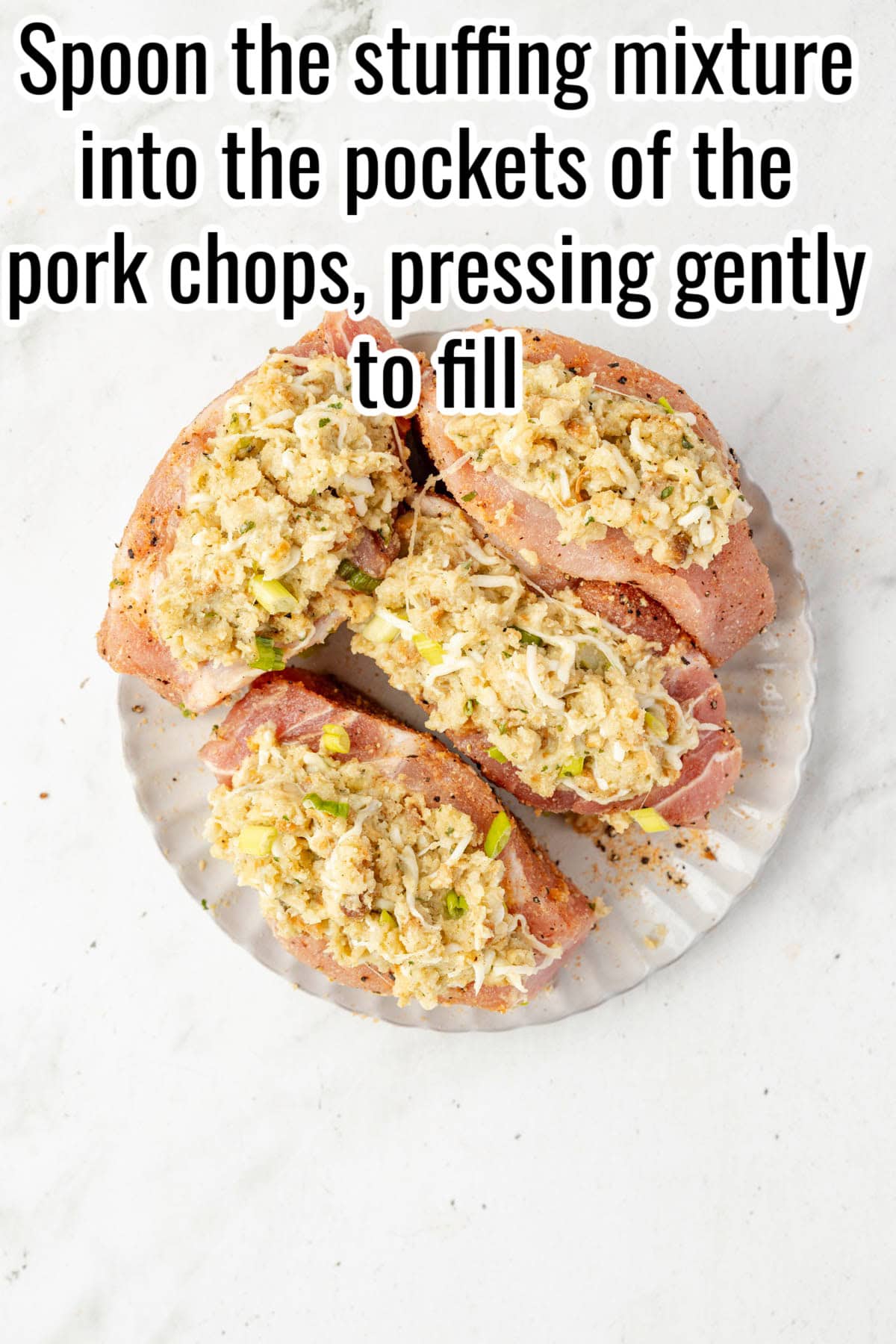 Raw pork chops filled with stuffing on a plate. Text on the image says 'Spoon the stuffing mixture into the pockets of the pork chops, pressing gently to fill'.