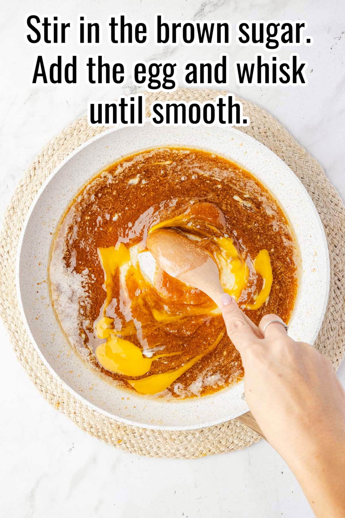 A hand stirs egg into brown sugar mixture in a skillet. Text on the image says 'Stir in the brown sugar. Add the egg and whisk until smooth'.