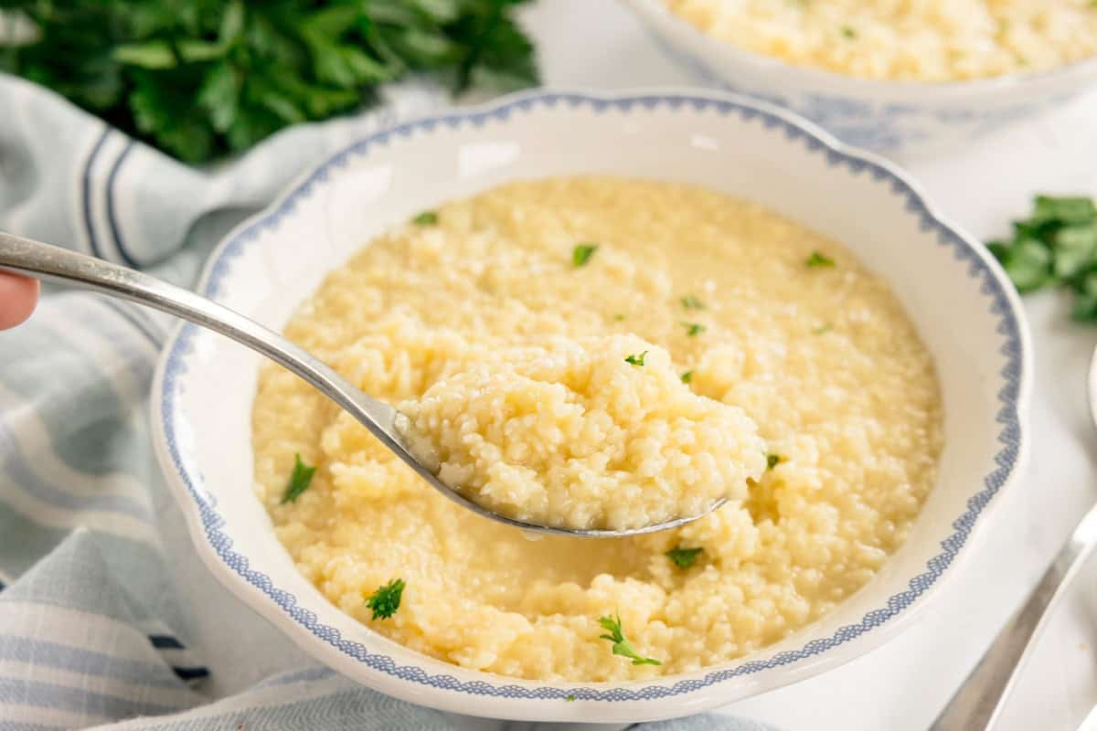 A spoonful of creamy pastina being lifted from a bowl, topped with parsley.