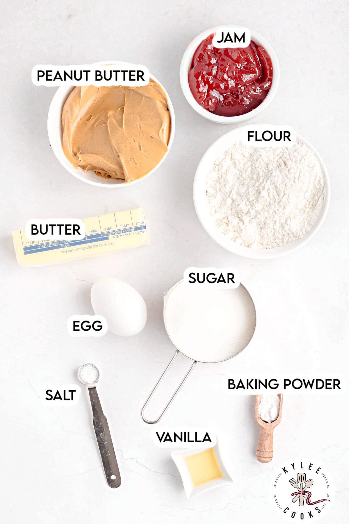 Bowls of peanut butter, jam, flour, sugar, butter, egg, salt, vanilla, and baking powder labeled. Text on the image says 'PEANUT BUTTER', 'JAM', 'FLOUR', 'BUTTER', 'EGG', 'SUGAR', 'SALT', 'VANILLA', 'BAKING POWDER'.