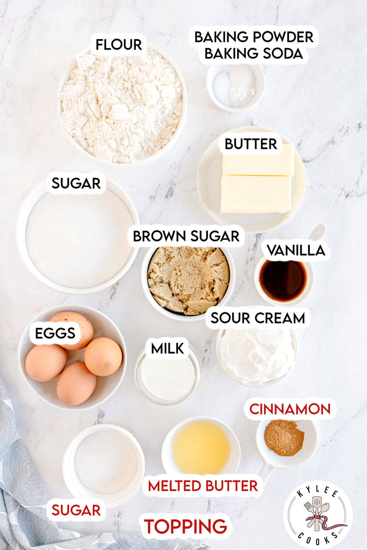 Bowls of flour, sugars, butter, eggs, and other labeled ingredients for snickerdoodle bundt cake. Text on the image says 'FLOUR', 'SUGAR', 'BROWN SUGAR', 'EGGS', 'VANILLA', 'BUTTER', 'SOUR CREAM', 'CINNAMON', 'BAKING POWDER BAKING SODA', 'MILK', 'MELTED BUTTER', 'TOPPING'.