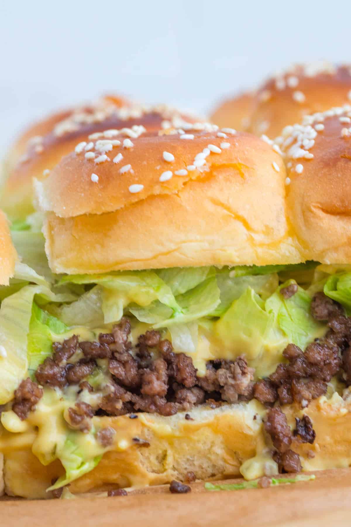 Sliders made with sesame seed buns, shredded lettuce, ground beef, and melted cheese.