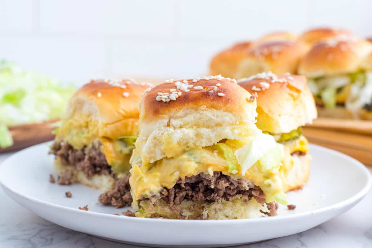 Two sliders on a white plate showing layers of ground beef, cheese, pickles, and lettuce.