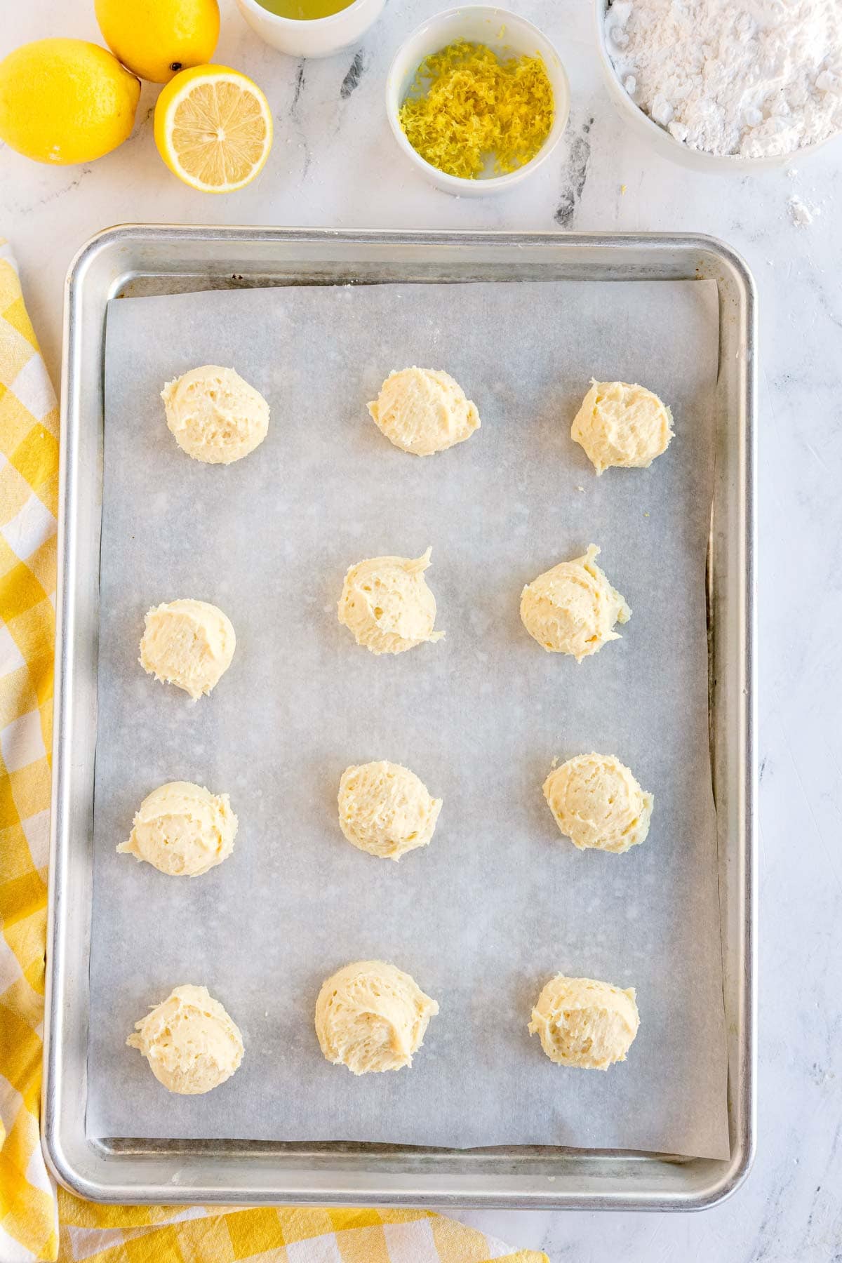 Scoops of lemon cookie dough arranged on a parchment-lined baking sheet.