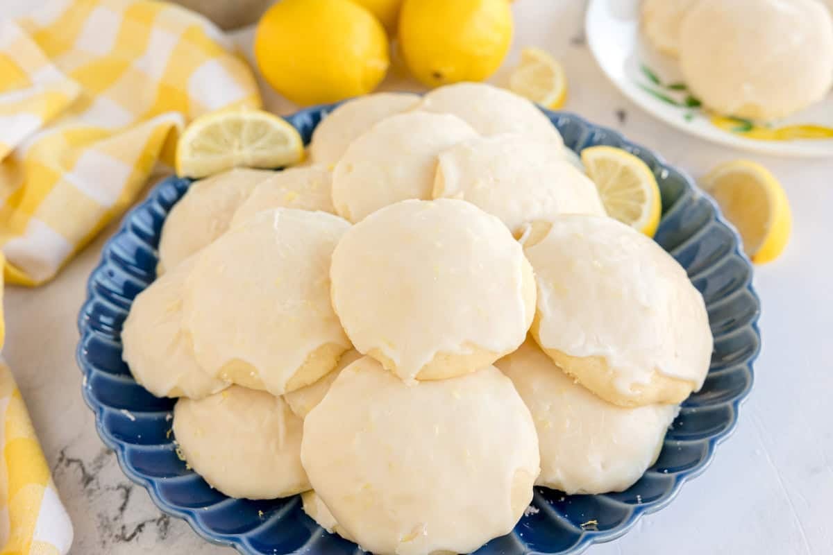 A blue plate stacked with glazed lemon cookies and lemon slices.