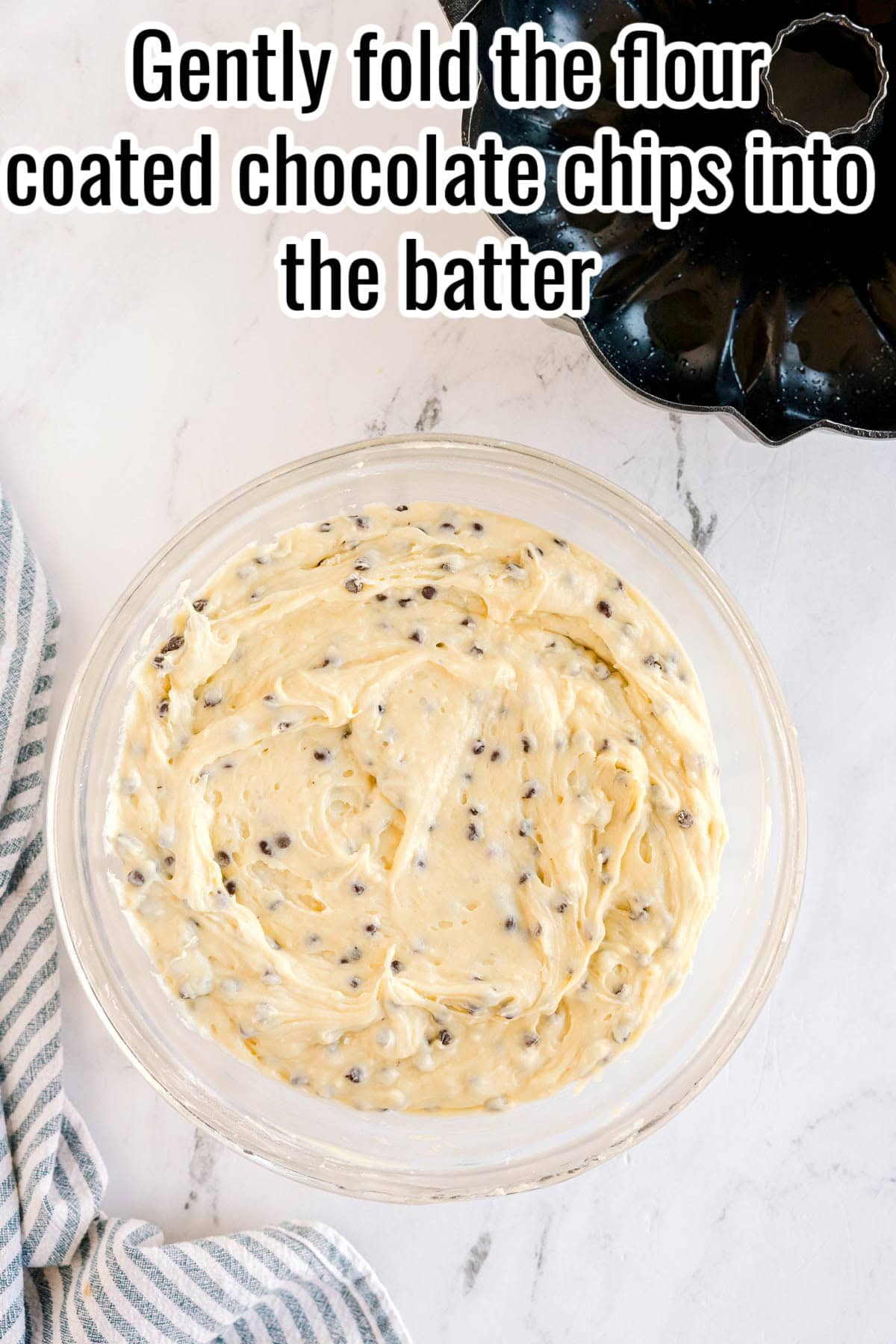 A glass bowl filled with chocolate chip cake batter. Text on the image says 'Gently fold the flour coated chocolate chips into the batter'.