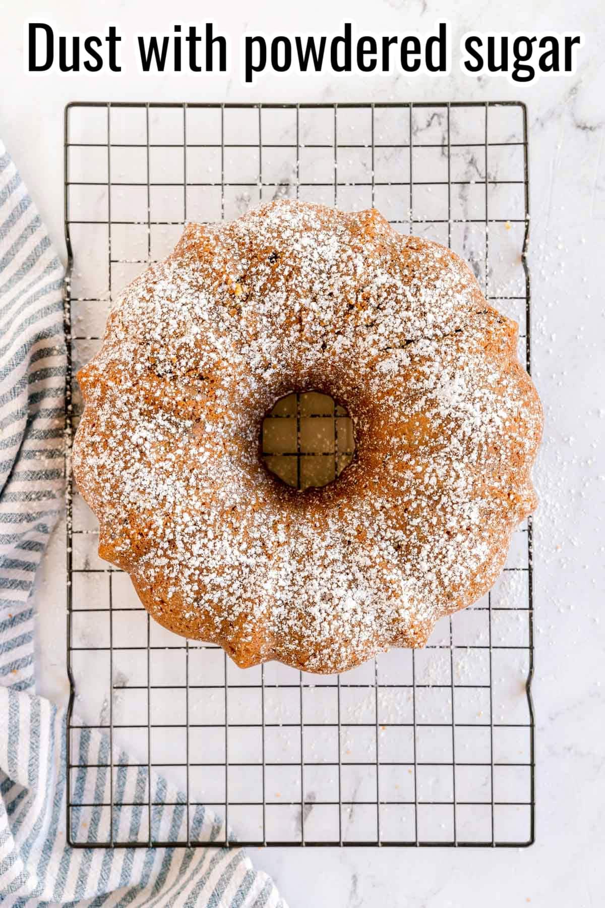 Bundt cake on a wire rack dusted with powdered sugar. Text on the image says 'Dust with powdered sugar'.
