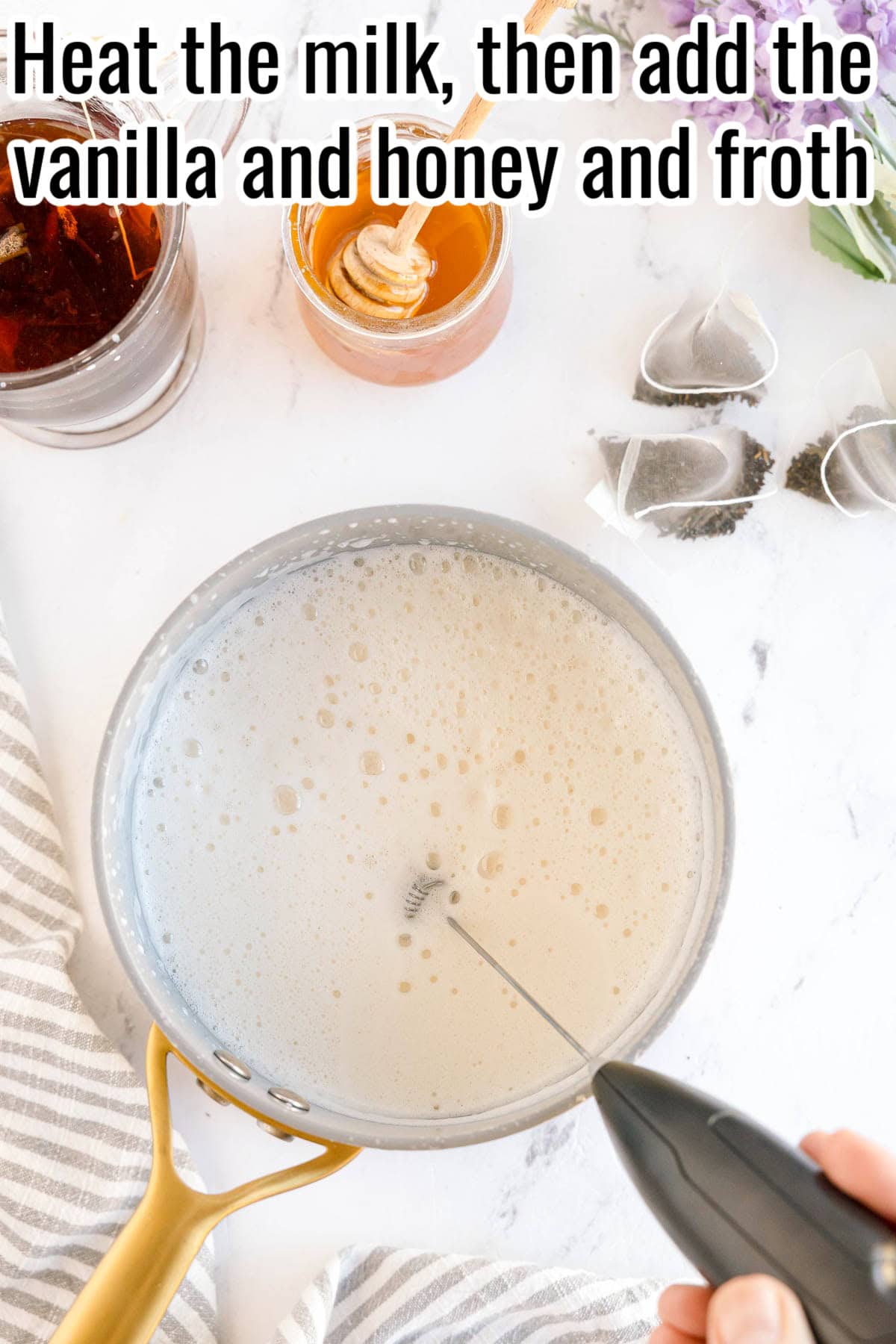 A saucepan of foamy milk with a frother. Honey and vanilla nearby. Text on the image says 'Heat the milk, then add the vanilla and honey and froth'.