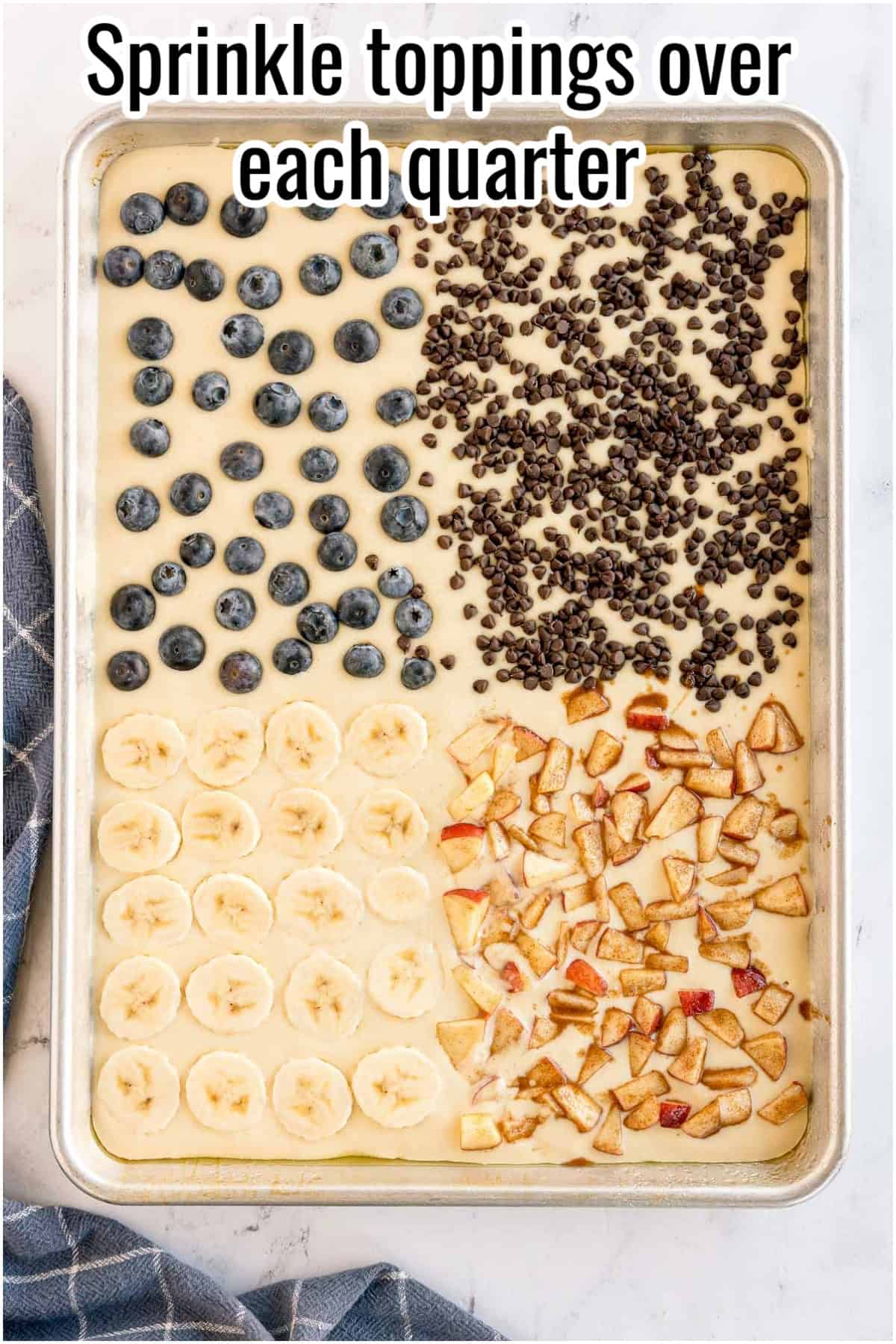 Sheet pan with pancake batter topped in four quarters with chocolate chips, apples, bananas, and blueberries. Text on the image says 'Sprinkle toppings over each quarter'.