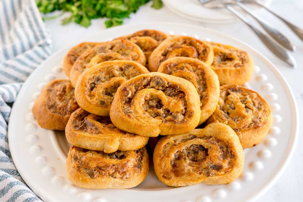 A white plate stacked with golden sausage pinwheels.