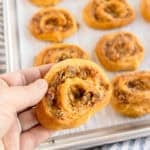 A hand holding a sausage pinwheel over a tray of more pinwheels.
