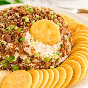 A cheese ball with a cracker dipped into the center, surrounded by a ring of round crackers.