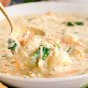 A gold spoon lifting creamy chicken gnocchi soup with spinach and shredded carrots.