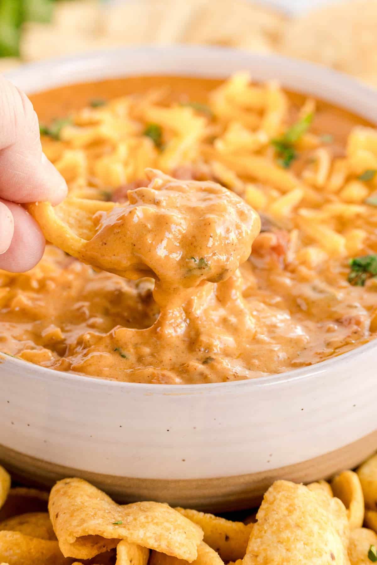 A corn chip scooping thick chili cheese dip from a bowl.
