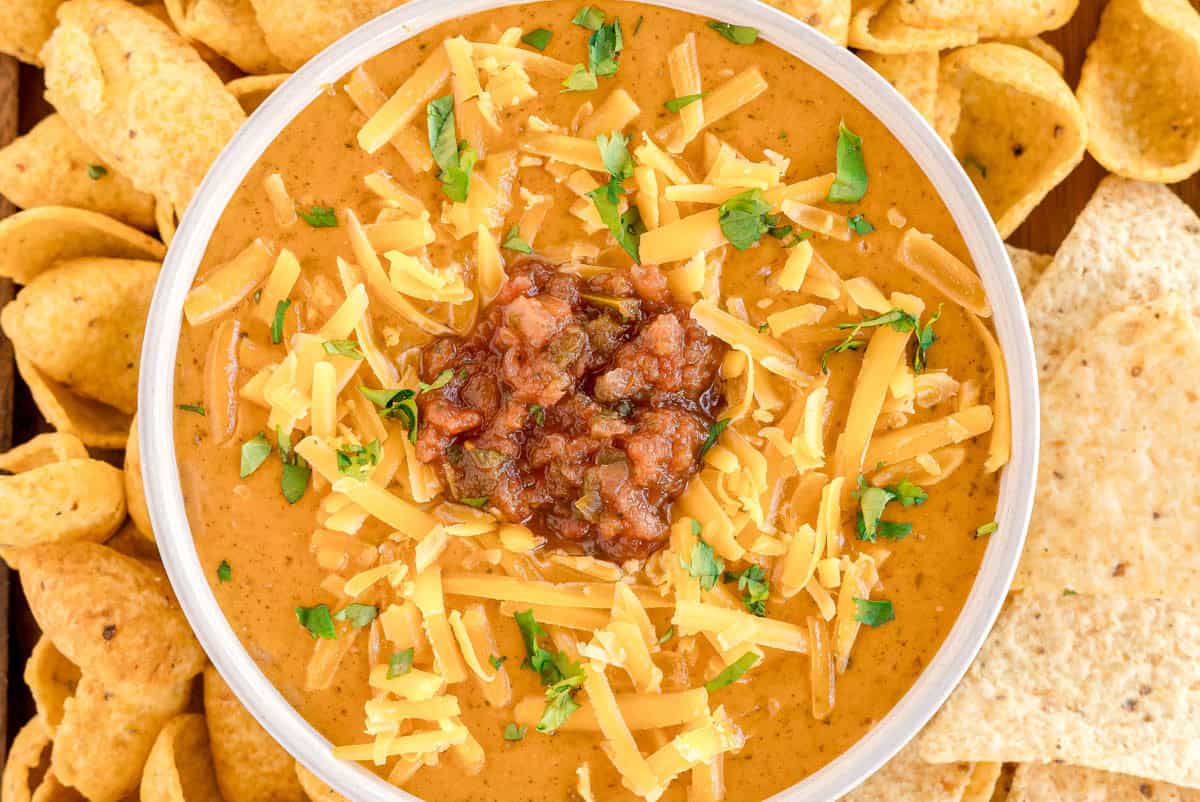 A bowl of chili cheese dip topped with shredded cheddar, salsa, and cilantro.