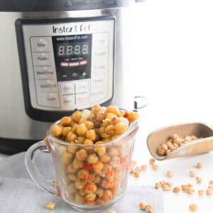 Cooked chickpeas in a glass measuring cup in front of an Instant Pot.