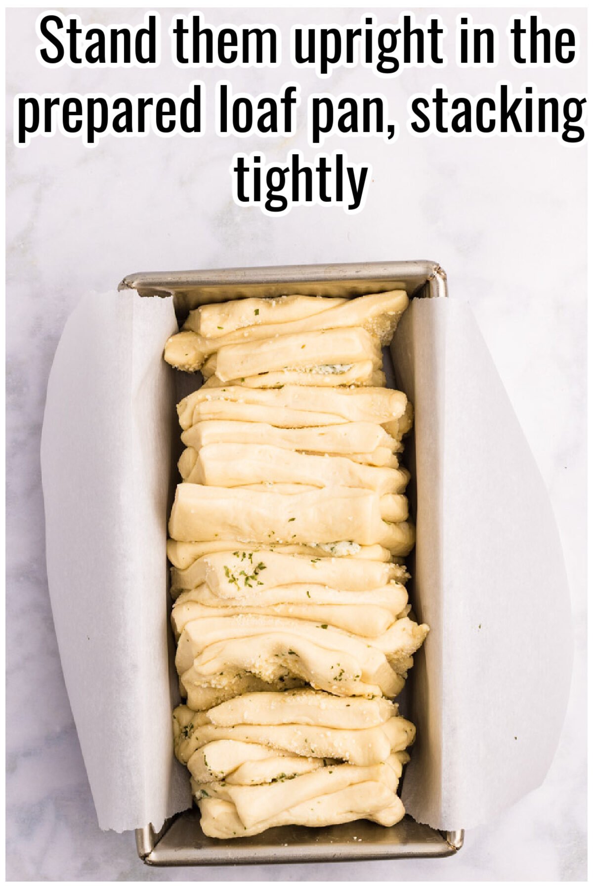 Folded dough pieces stacked upright in a loaf pan. Text on the image says 'Stand them upright in the prepared loaf pan, stacking tightly'.
