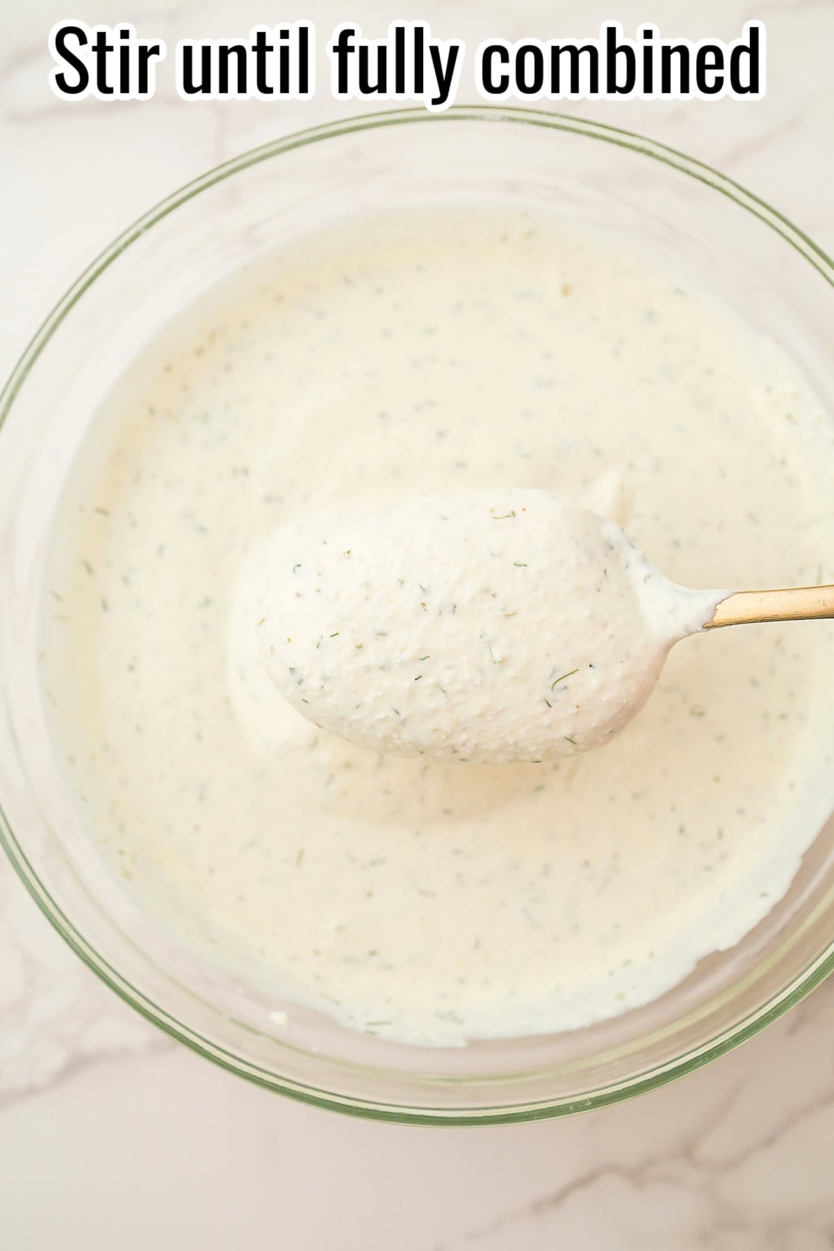 A spoonful of creamy dill dip over a bowl of dip. Text on the image says 'Stir until fully combined'.