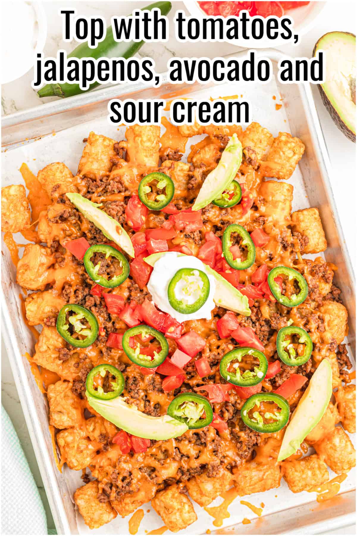 A tray of totchos topped with melted cheese, diced tomatoes, sliced jalapeños, avocado slices, and sour cream. Text on the image says 'Top with tomatoes, jalapeños, avocado and sour cream'.