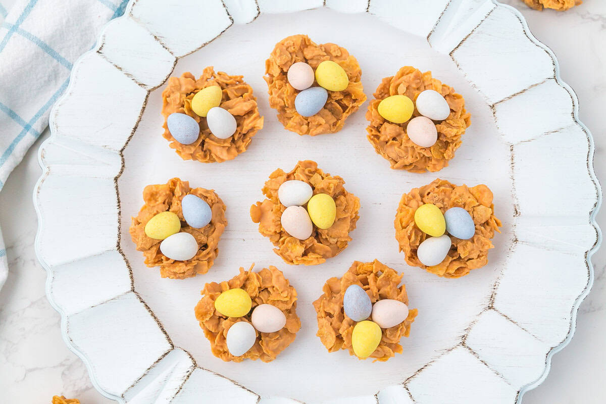 Eight bird’s nest cookies with pastel candy eggs arranged on a white platter.
