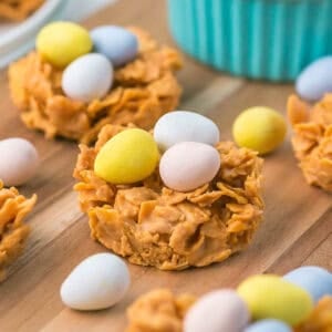Close up bird’s nest cookie topped with three pastel candy eggs on a wooden board.