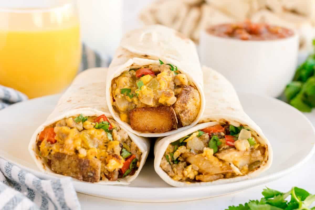 Three breakfast burritos cut in half showing sausage, potatoes, eggs, cheese, and peppers inside.