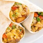Close-up of breakfast burritos cut open, filled with sausage, potatoes, scrambled eggs, cheese, and red bell peppers.