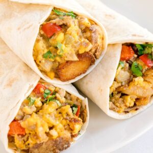 Close-up of breakfast burritos cut open, filled with sausage, potatoes, scrambled eggs, cheese, and red bell peppers.