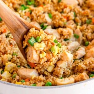 Close up of chicken fried rice with chicken, peas, carrots, and scrambled eggs in a pan.