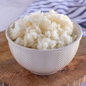 A white ceramic bowl filled with cooked white rice sits on a wooden surface, showcasing the perfect results from a reliable rice cooking guide.